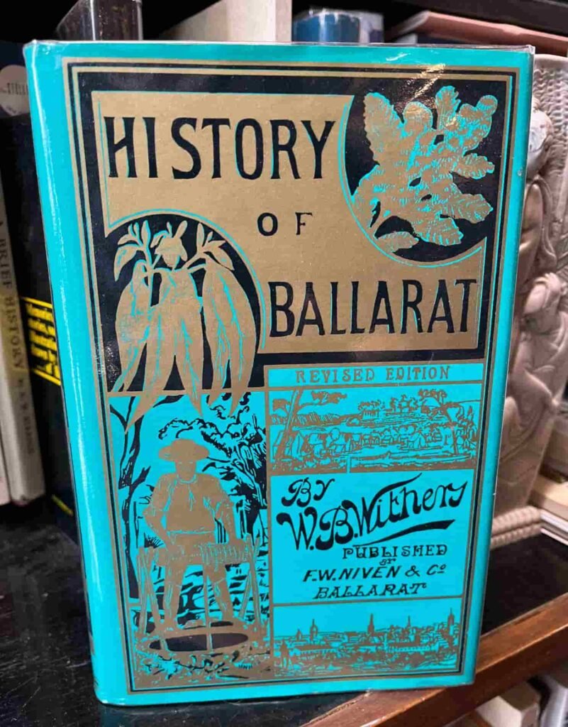 A vintage book titled History of Ballarat by W.B. Withers, Revised Edition. The cover features ornate illustrations of a miner, foliage, and the Ballarat landscape, set against a turquoise and gold color scheme
